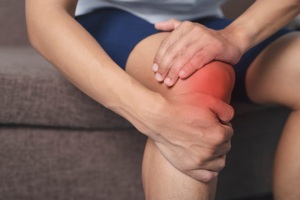A man grimaces in pain while holding his knee, indicating discomfort from a knee injury