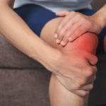 A man grimaces in pain while holding his knee, indicating discomfort from a knee injury