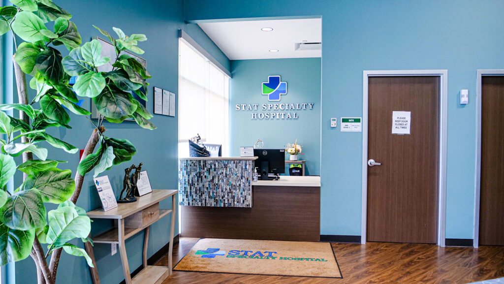 Reception area of STAT Specialty Hospital featuring a front desk, indoor plants, and a welcome mat with the hospital logo, creating a clean and welcoming environment.