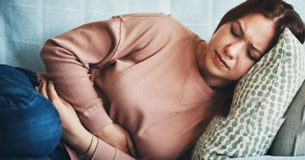 A woman lying on a couch, visibly in discomfort, possibly experiencing acid reflux symptoms.