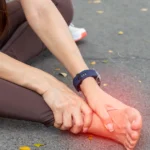 Person holding swollen foot with visible discomfort outdoors.