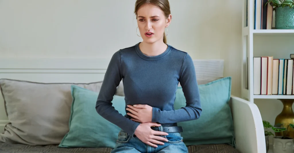 young-teenage-female-experiencing-abdominal-pain-sitting-couch-home