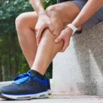 Man sitting outdoors holding his calf due to muscle pain.
