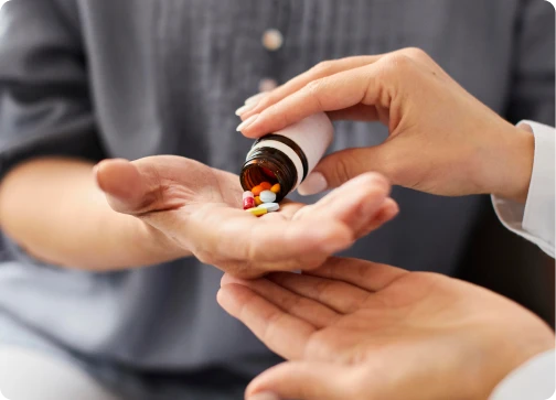 A close-up of a person’s hands pouring a variety of colorful pills from a brown prescription bottle into the open palm of another person.