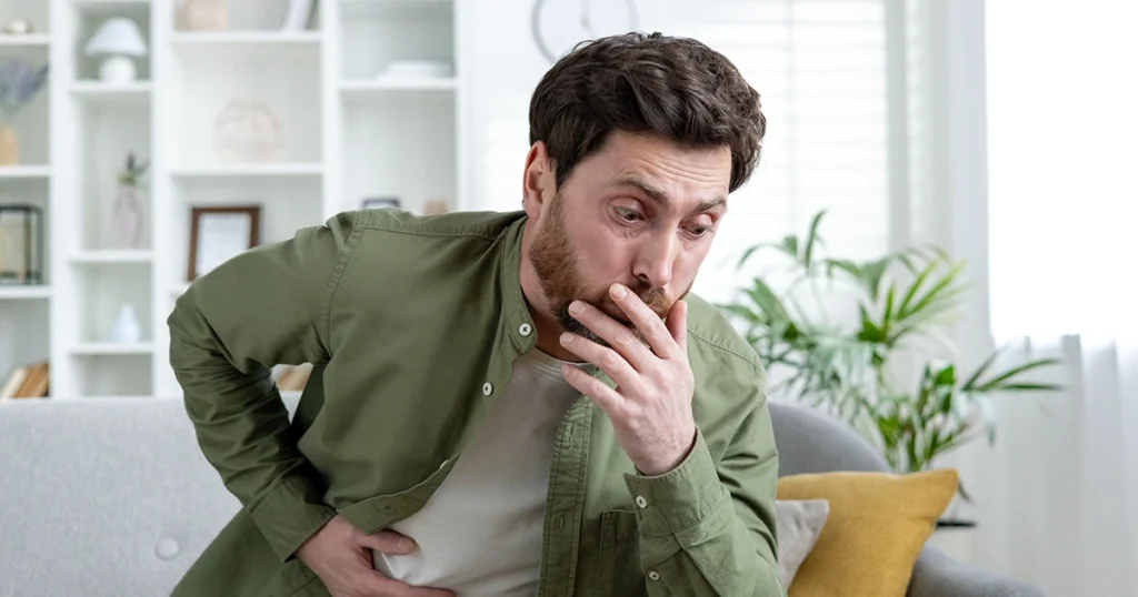Man holding his stomach and covering his mouth, feeling nauseous.