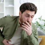 Man holding his stomach and covering his mouth, feeling nauseous.
