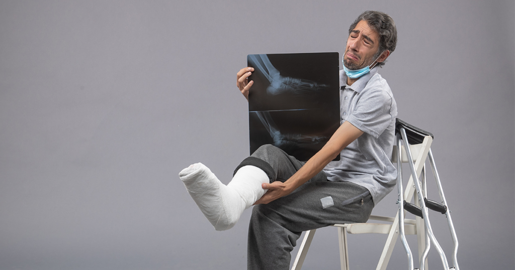 Man with a leg cast holding an X-ray while sitting with crutches.
