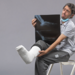 Man with a leg cast holding an X-ray while sitting with crutches.
