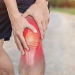 Person holding a painful knee with red inflammation highlight.