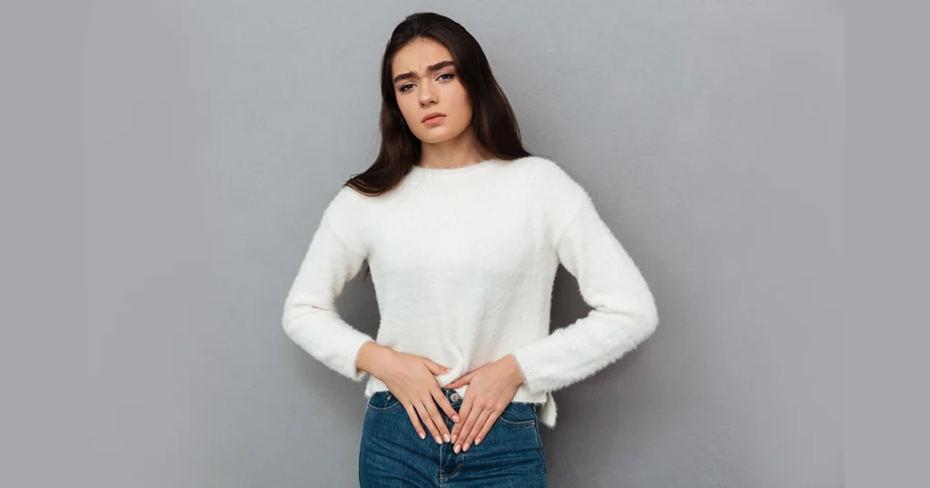 Young woman holding her lower abdomen in discomfort.