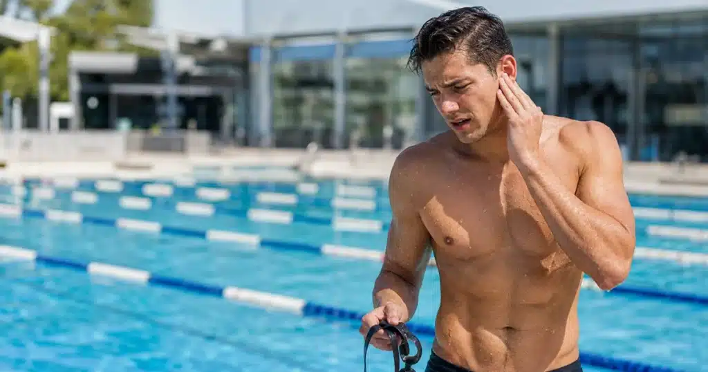 Swimmer holding his ear in pain beside a swimming pool.