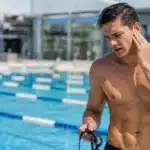 Swimmer holding his ear in pain beside a swimming pool.