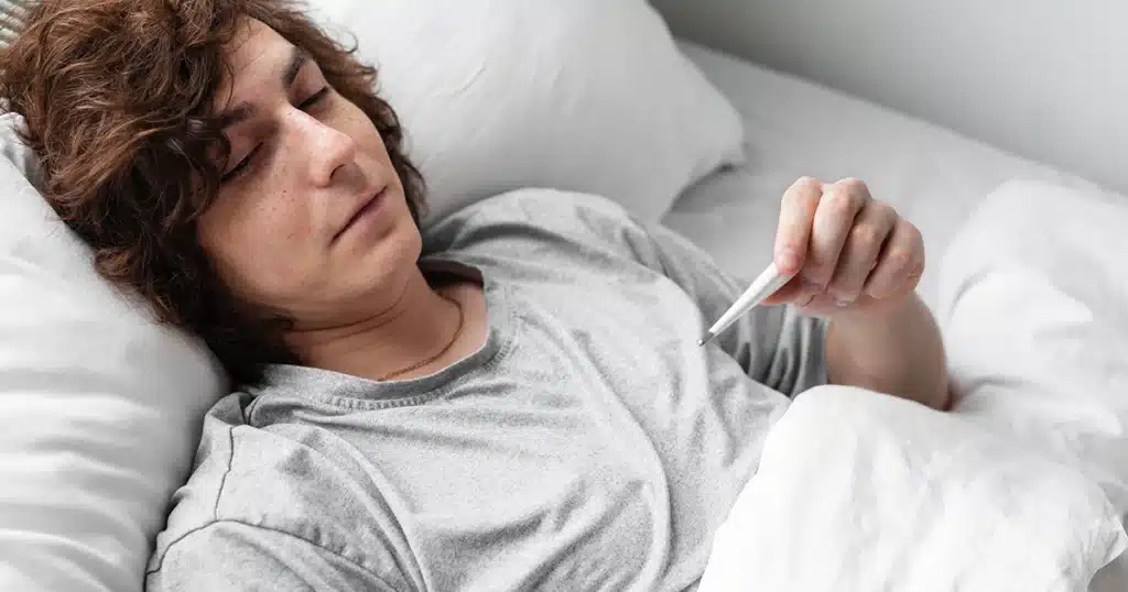 Sick young man checking his temperature in bed.