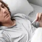 Sick young man checking his temperature in bed.