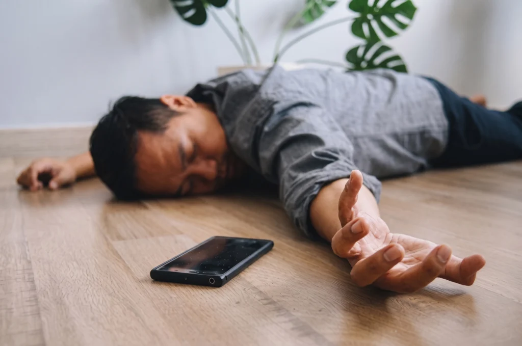 A man lying unconscious on the floor with a smartphone resting nearby.