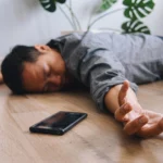 A man lying unconscious on the floor with a smartphone resting nearby.