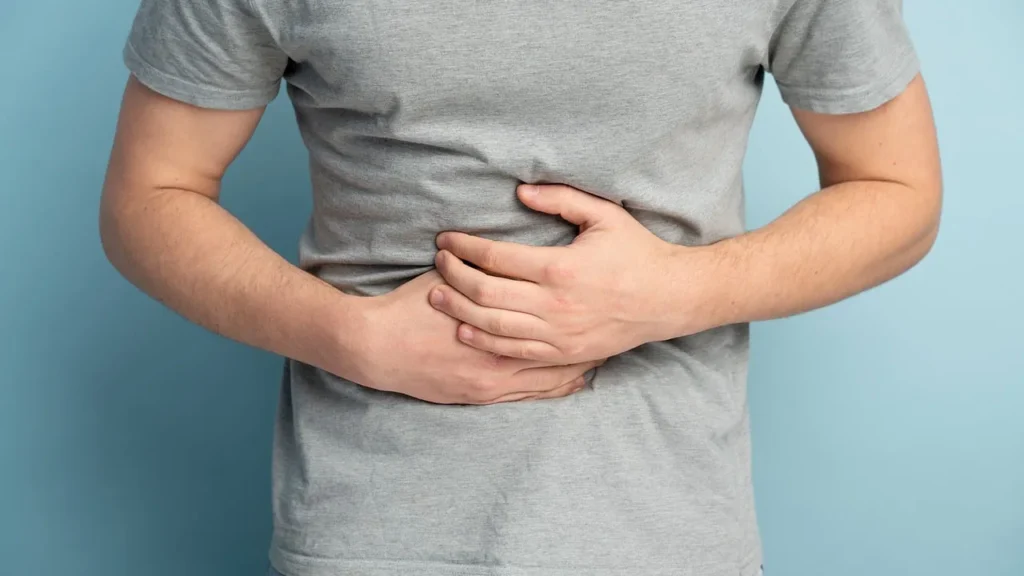 Man holding his stomach in discomfort against a light blue background.