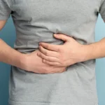 Man holding his stomach in discomfort against a light blue background.