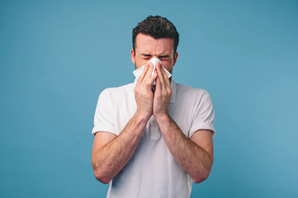 A man blowing his nose into a tissue against a blue background.