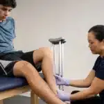 Sports Injuries: Physical therapist examines young male athlete's injured lower leg and ankle.