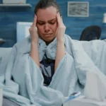 Sick woman wrapped in blanket holds head during painful headache.