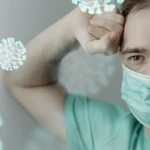 Exhausted man wearing a mask surrounded by viral particles.
