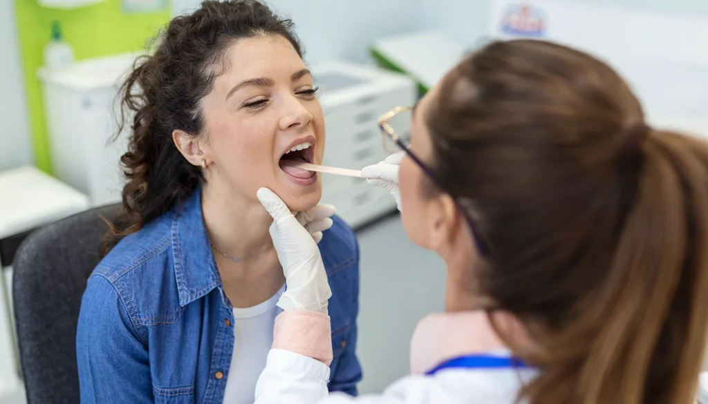 Female doctor uses tongue depressor to inspect patient's throat.