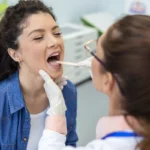Female doctor uses tongue depressor to inspect patient's throat.